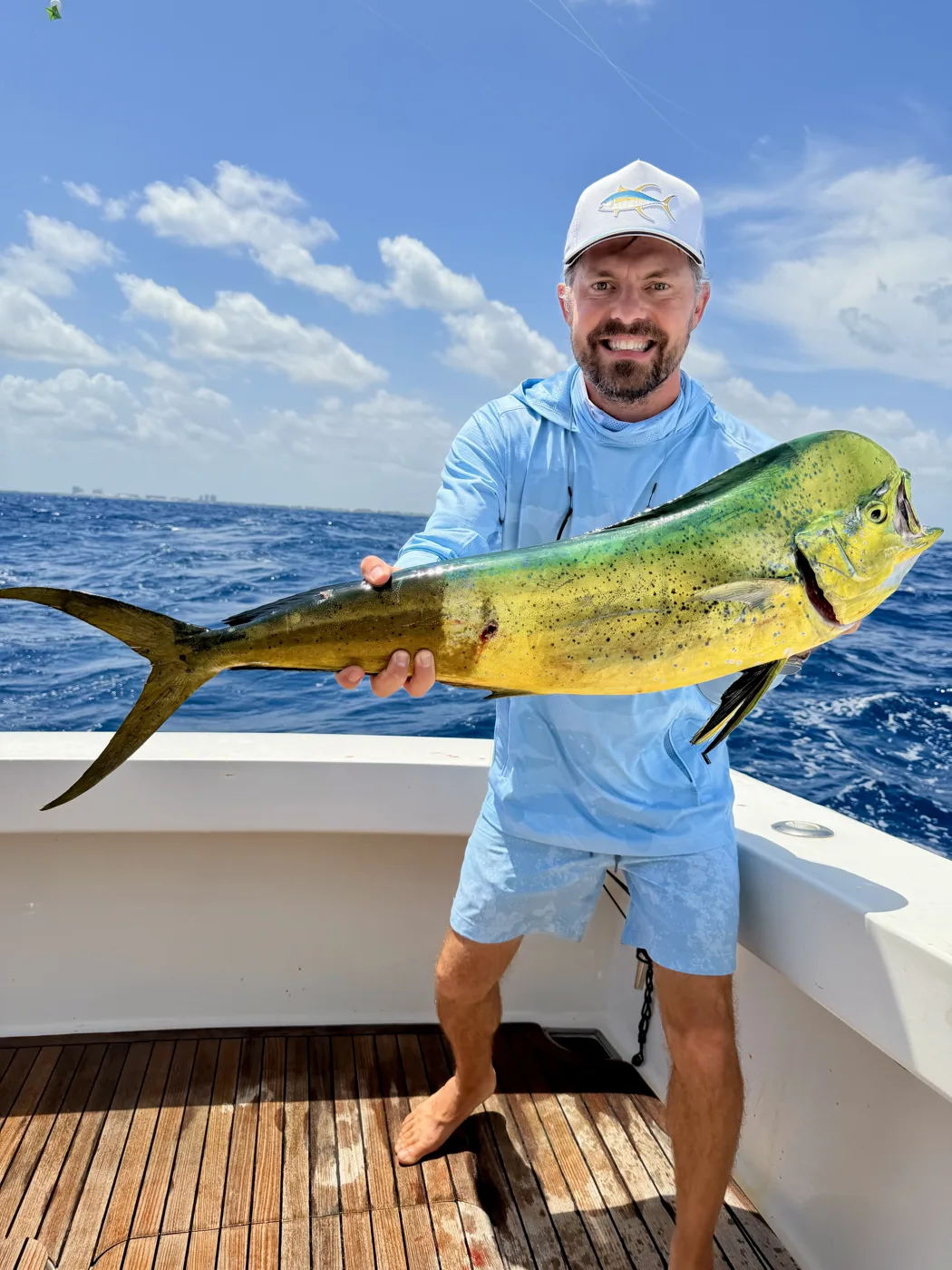 A mahi mahi held across the transom of a boat offshore, its flank still lit up green and gold